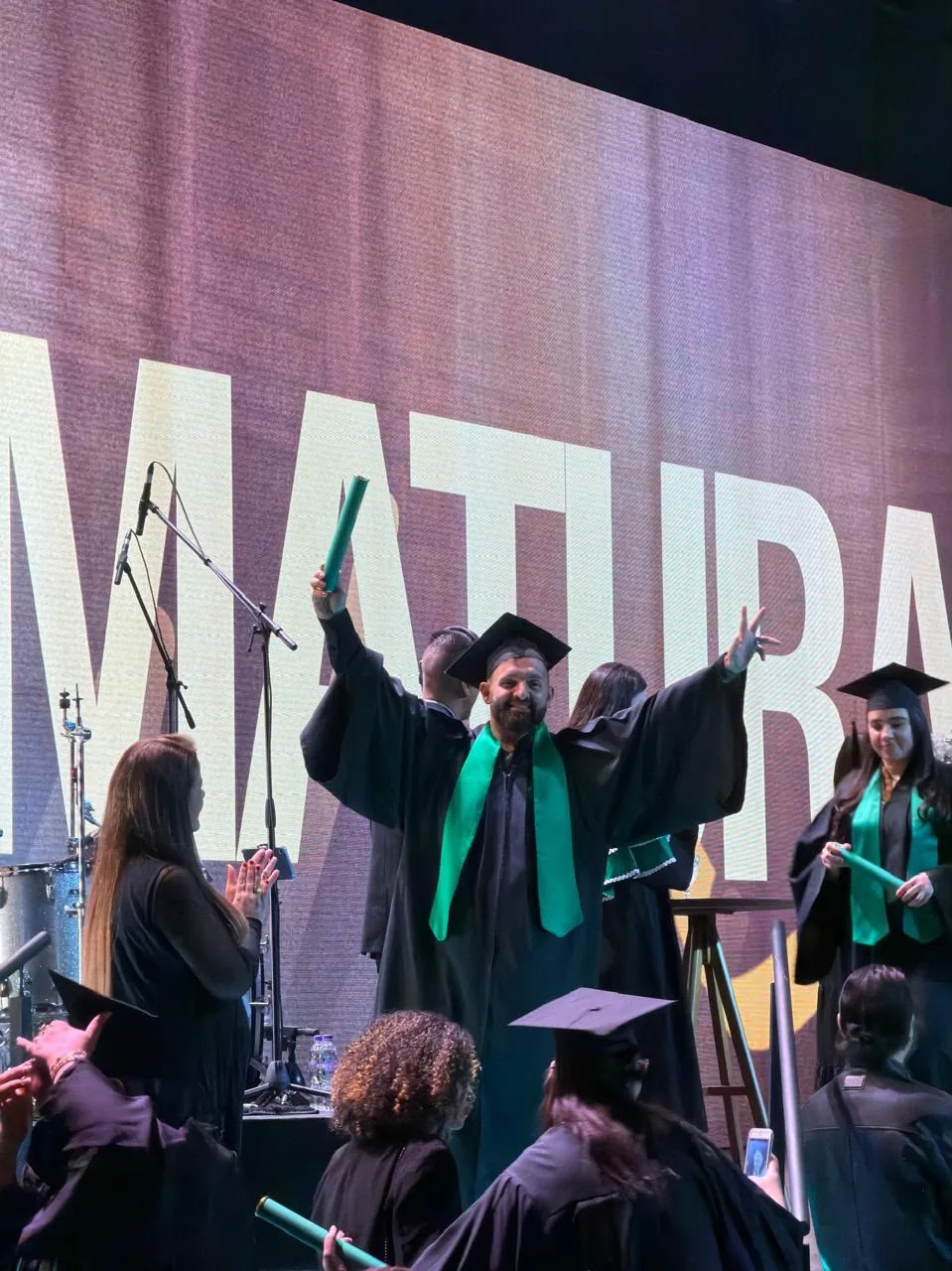 Evaldo Claro de beca e capelo, com os braços erguidos durante a formatura.